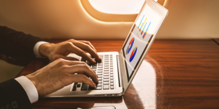 Man in a white shirt and black suit jacket on his laptop looking at his portfolio online while on a plane.