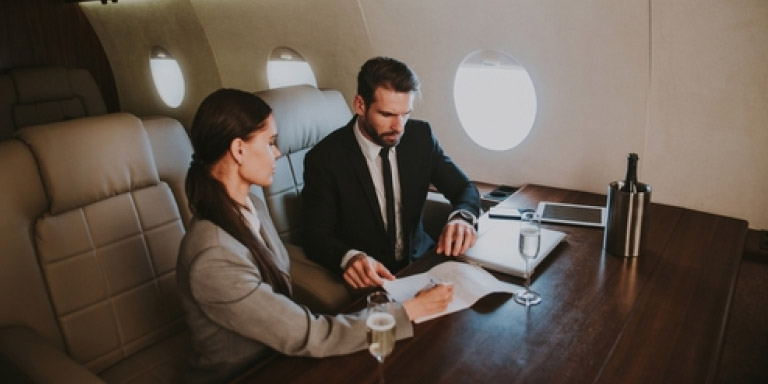 Lady and man sitting in a private jet looking at offshore investment projections so that they can help their clients make the best decisions for their portfolios.